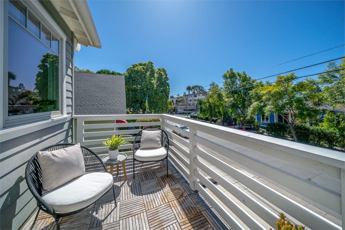 A sunny guest balcony with café seating overlooking a leafy San Luis Obispo street