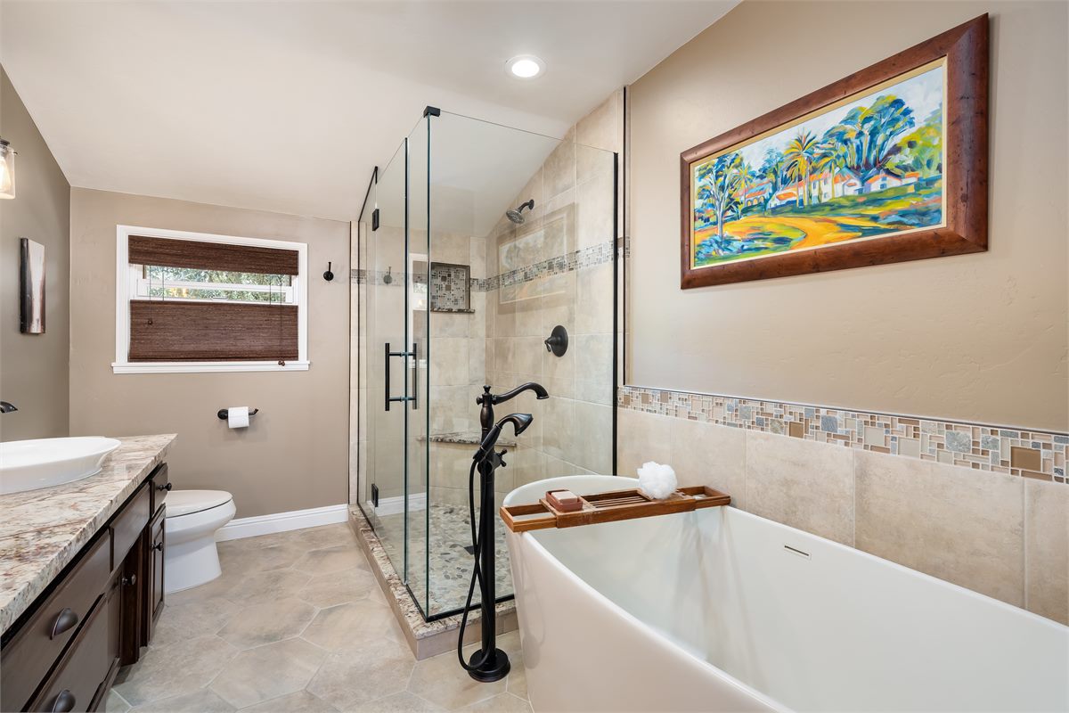 A styled primary bathroom with a freestanding tub, bath tray and artwork, ready for photos